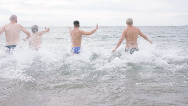 A group of LGBTQ friends playfully run into the beautiful crystal clear waters while at the beach on vacation. 