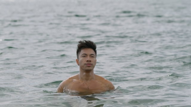 A stunning asian man exits the crystal clear water on a beach during the perfect holiday.
