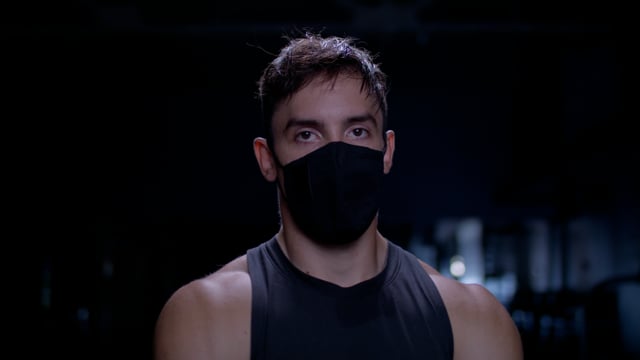 Strong and intense portrait of a focused and determined male athlete with a mask on at the gym. 
