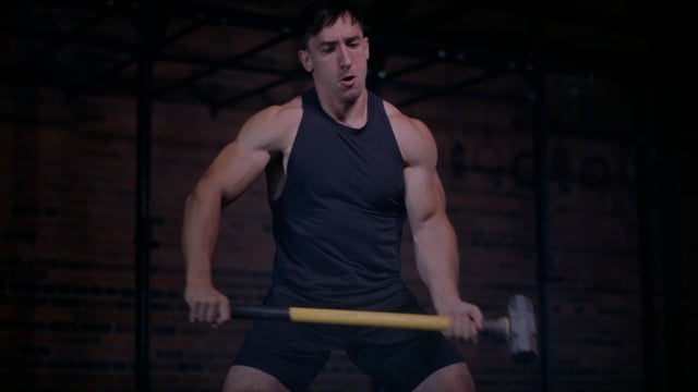 Strong and capable male athlete hammering tractor tire with sledge hammer as exercise. 