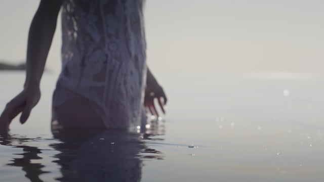A beautiful young lady plays with the surface of the water at sunset. 