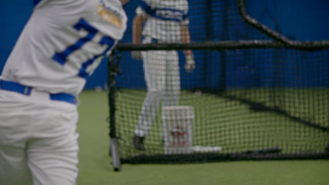 Athletic baseball player practising his swing in a training facility. 
