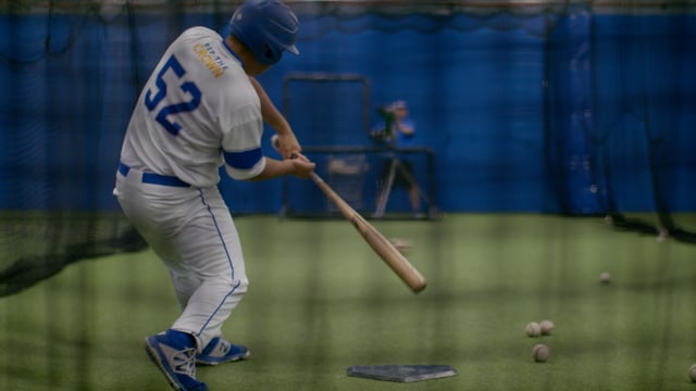 Athletic baseball player practising his swing in a training facility. 