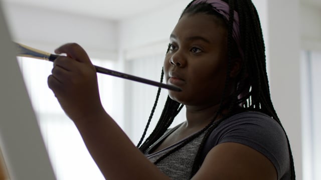 A young black female artist paints a beautiful canvas in her studio. 