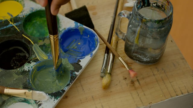 An artist's tools. Brushes, paints and palettes lay strewn about. 