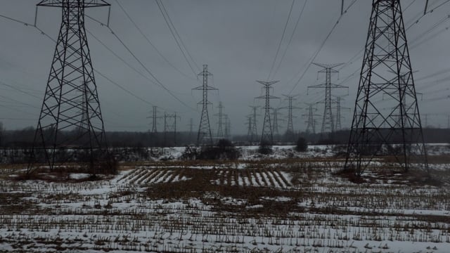 Endless stretch of hydropower lines carving a path across a muddy field in the rain.
