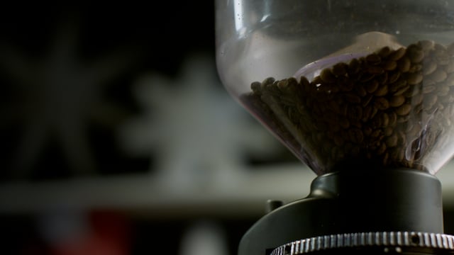 Hopper full of fresh coffee beans, slowly being ground. 