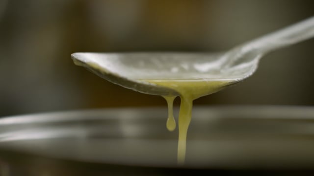 A large spoonful of fresh melted butter is lifted from the pot. 