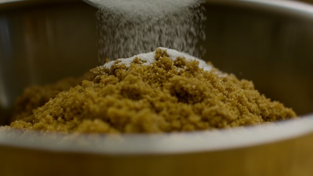 Granulated white sugar is added to the brown sugar as a sweet treat is being prepared. 