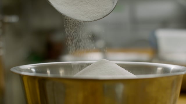A mountain of white sugar is added to the mixing bowl as a sweet treat is prepared. 
