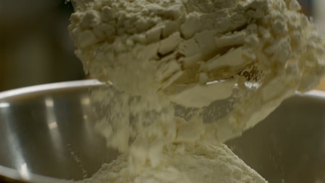 Large scoops of white flour are added to the mixing bowl in preparation of baking. 