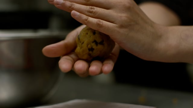 The baker rolls the decadent cookie dough into the perfect ball, ready to be baked. 
