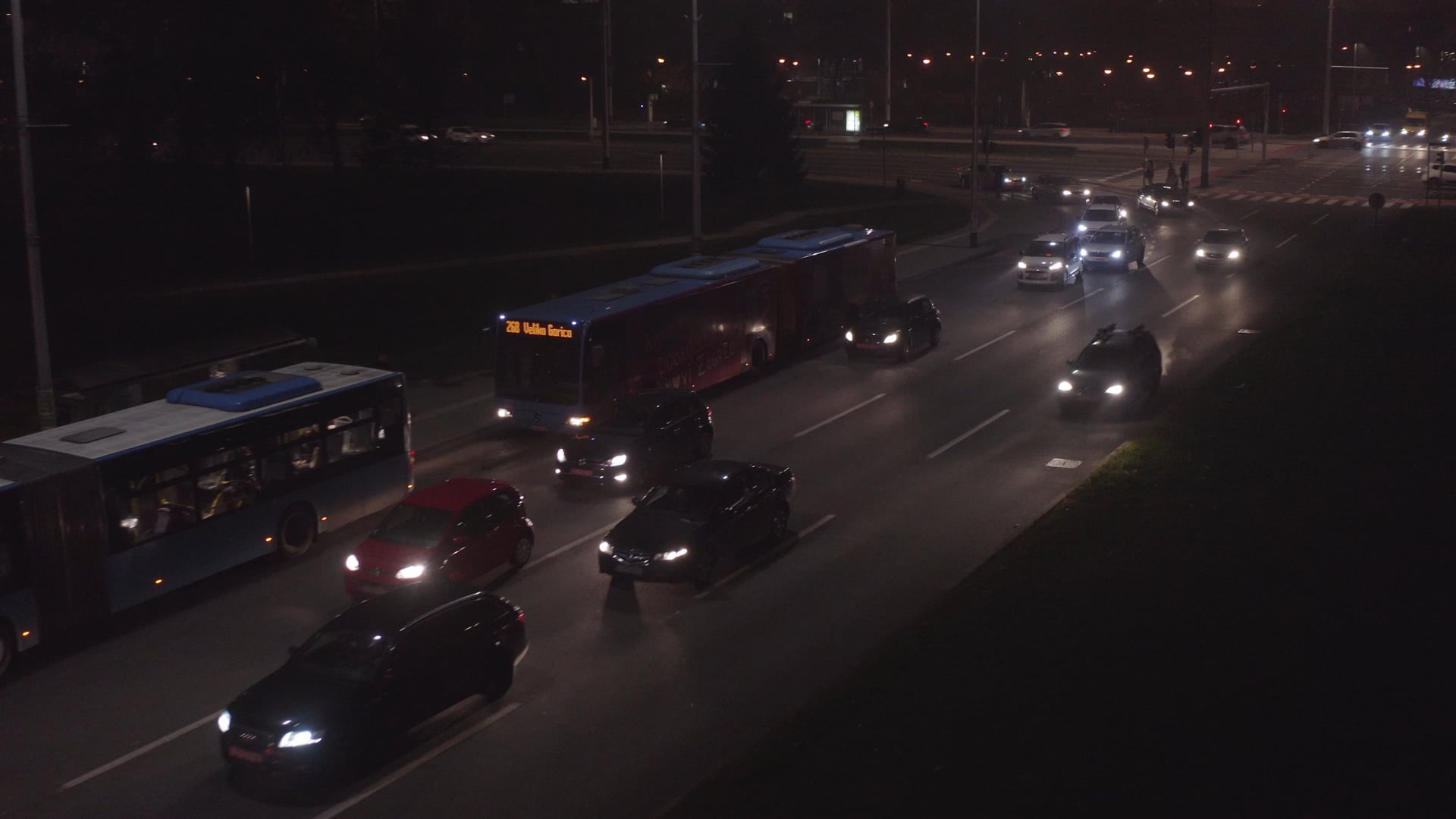 Night traffic, camera moving contrary to the traffic, buses waiting on the bus station