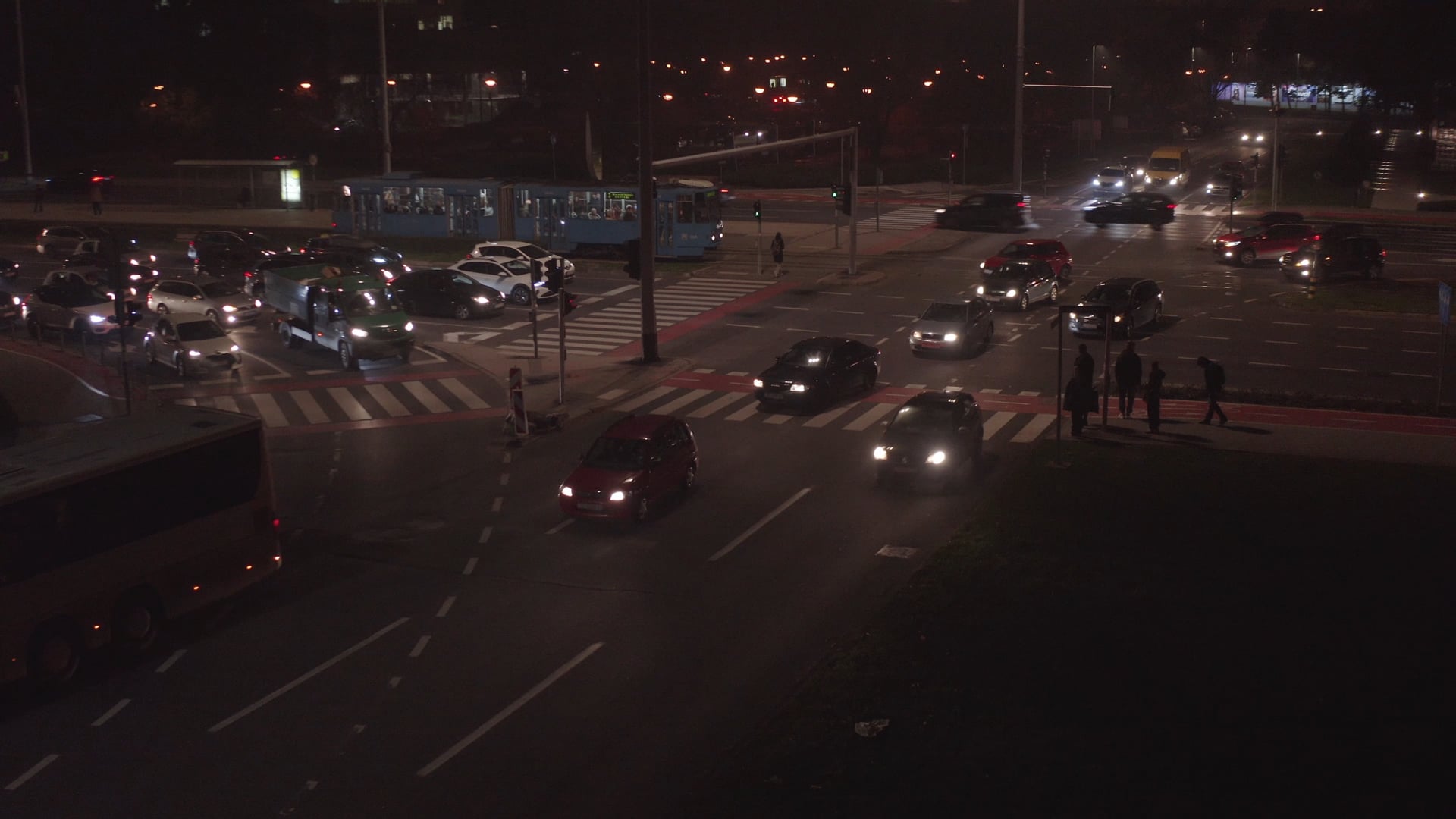 Night traffic, people waiting to cross the road on the pedestrian crossing, tram waiting for the green light in the background