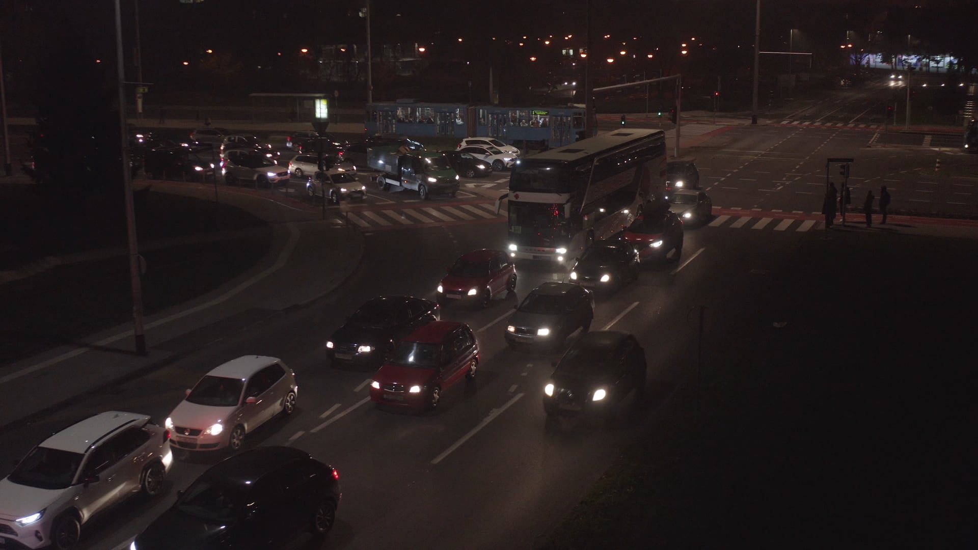 Night traffic, bus stuck in traffic jam, tram visible in the background, people walking on the pedestrian crossing