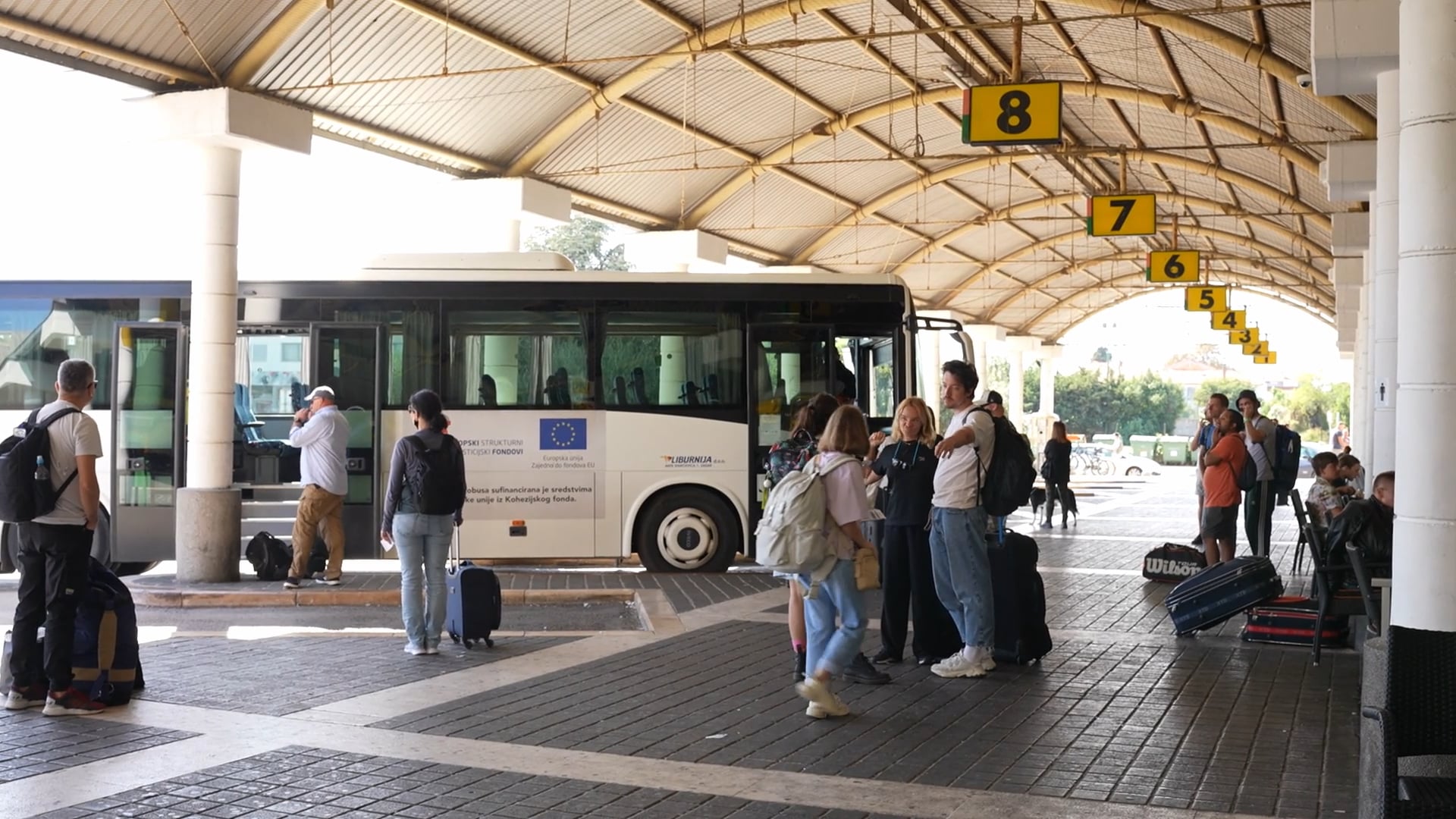 People waiting on the bus terminal, two people hugging