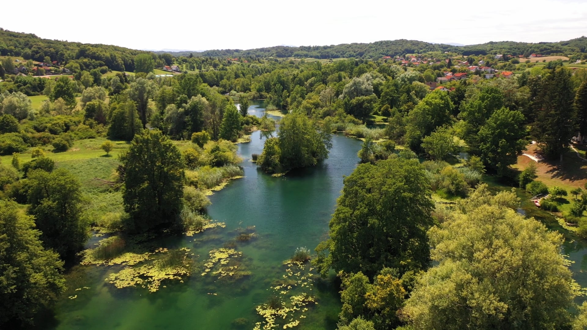 Beautiful green scenery, small crystal clear river, few houses visible, small waterfalls, prolonged shot