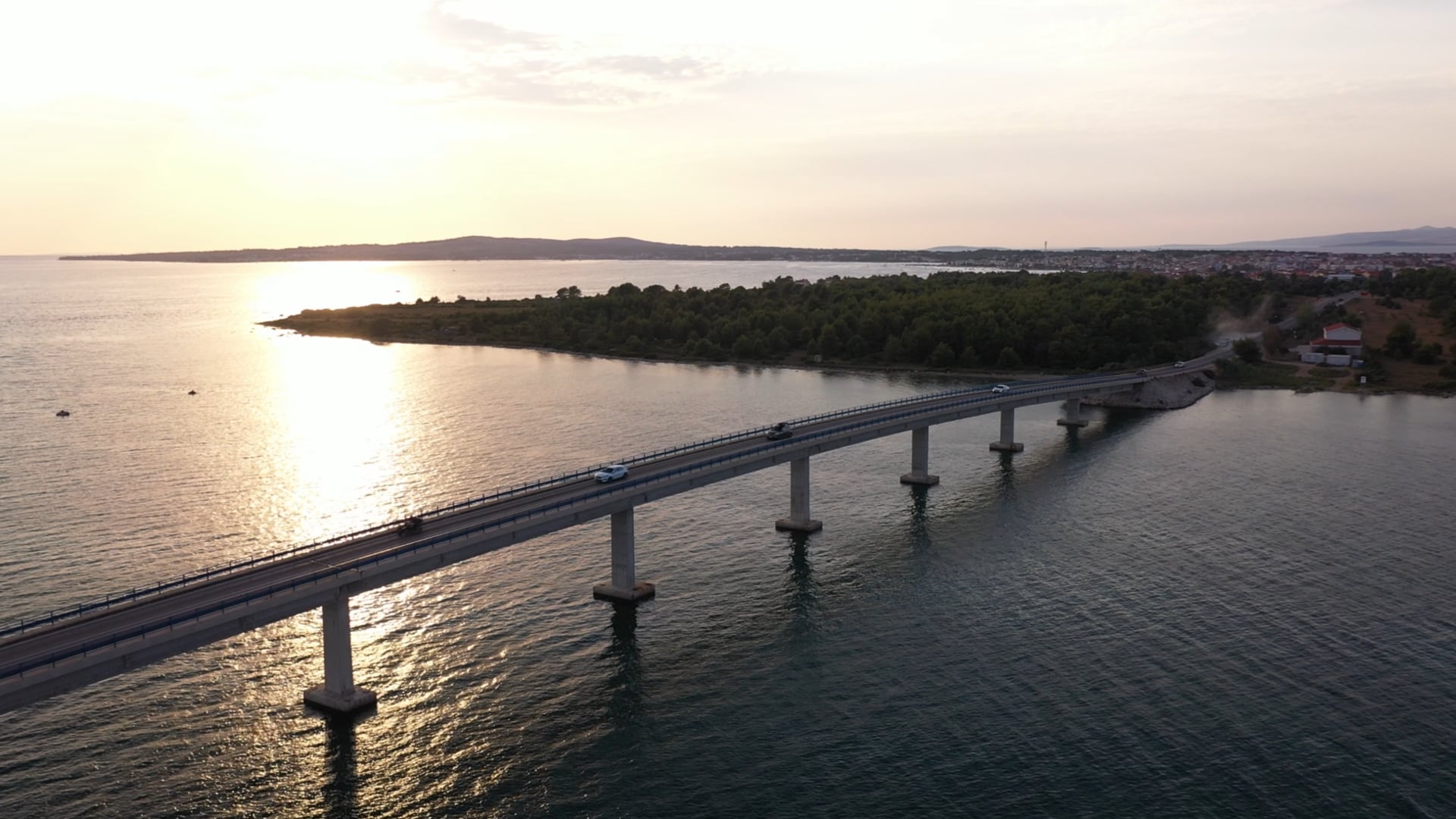 Cars driving on the bridge across the dark blue sea, sun shining, panned view