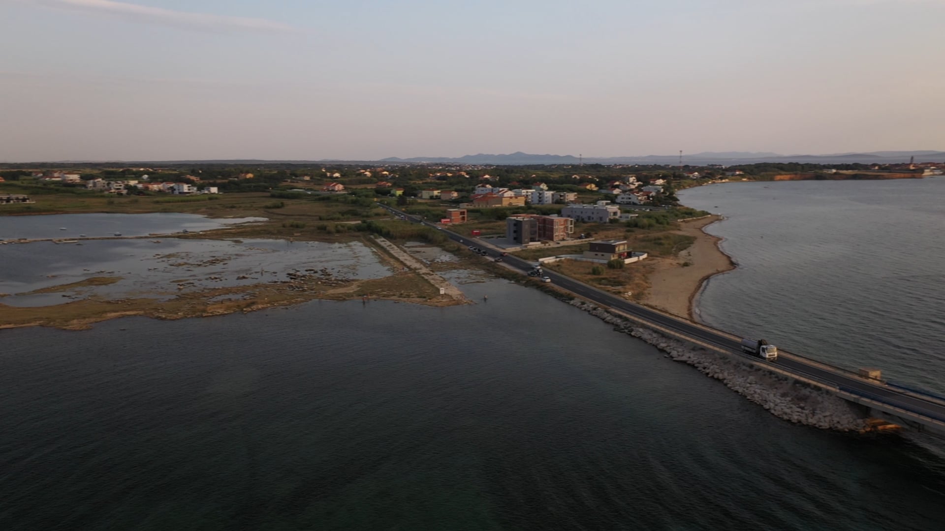 Truck driving on the bridge across the sea, sun shining in the bacground, panned view