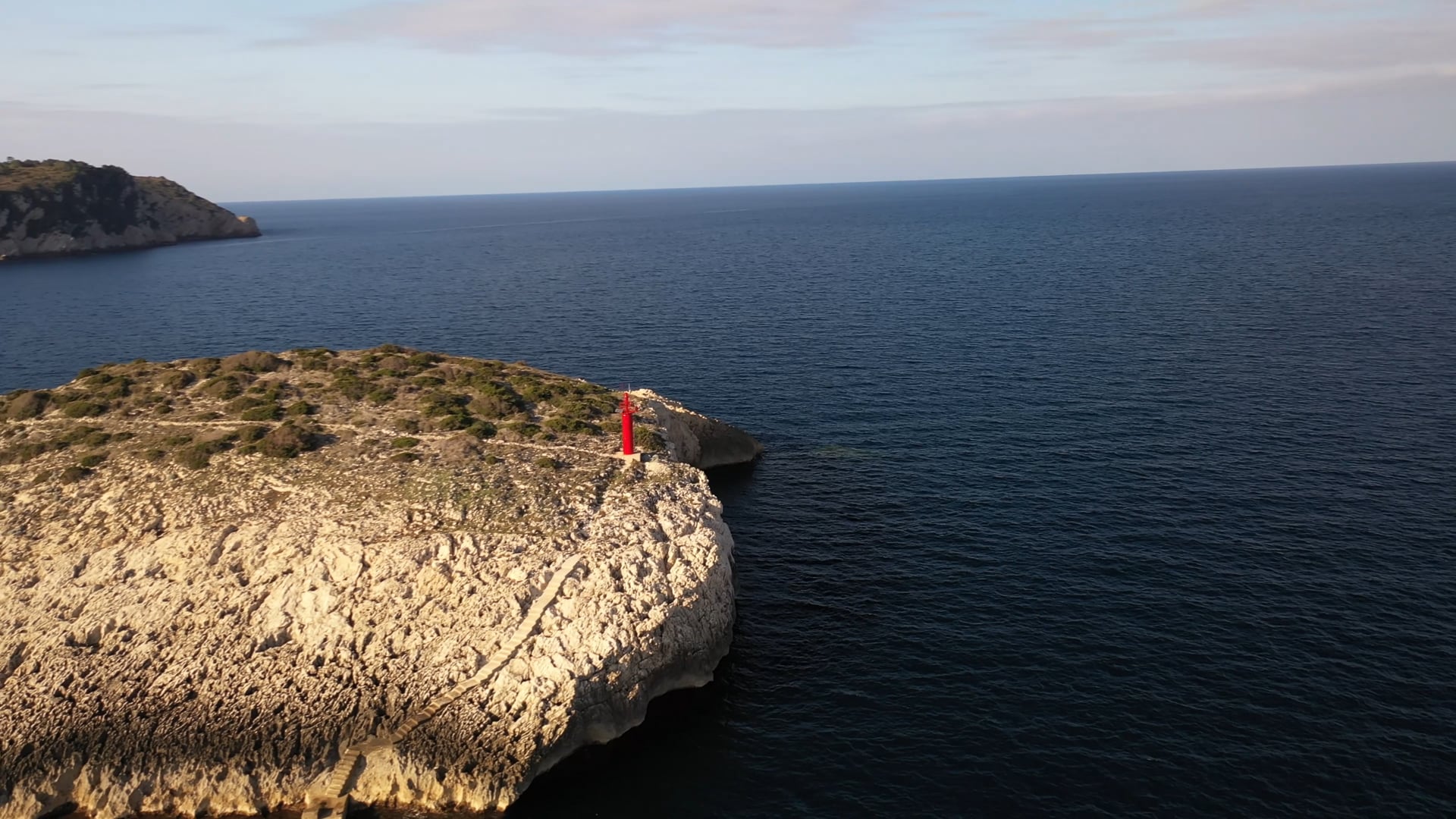 Small red lighthouse on the stone cliff, deep blue, calm sea, 360° view, sunshine