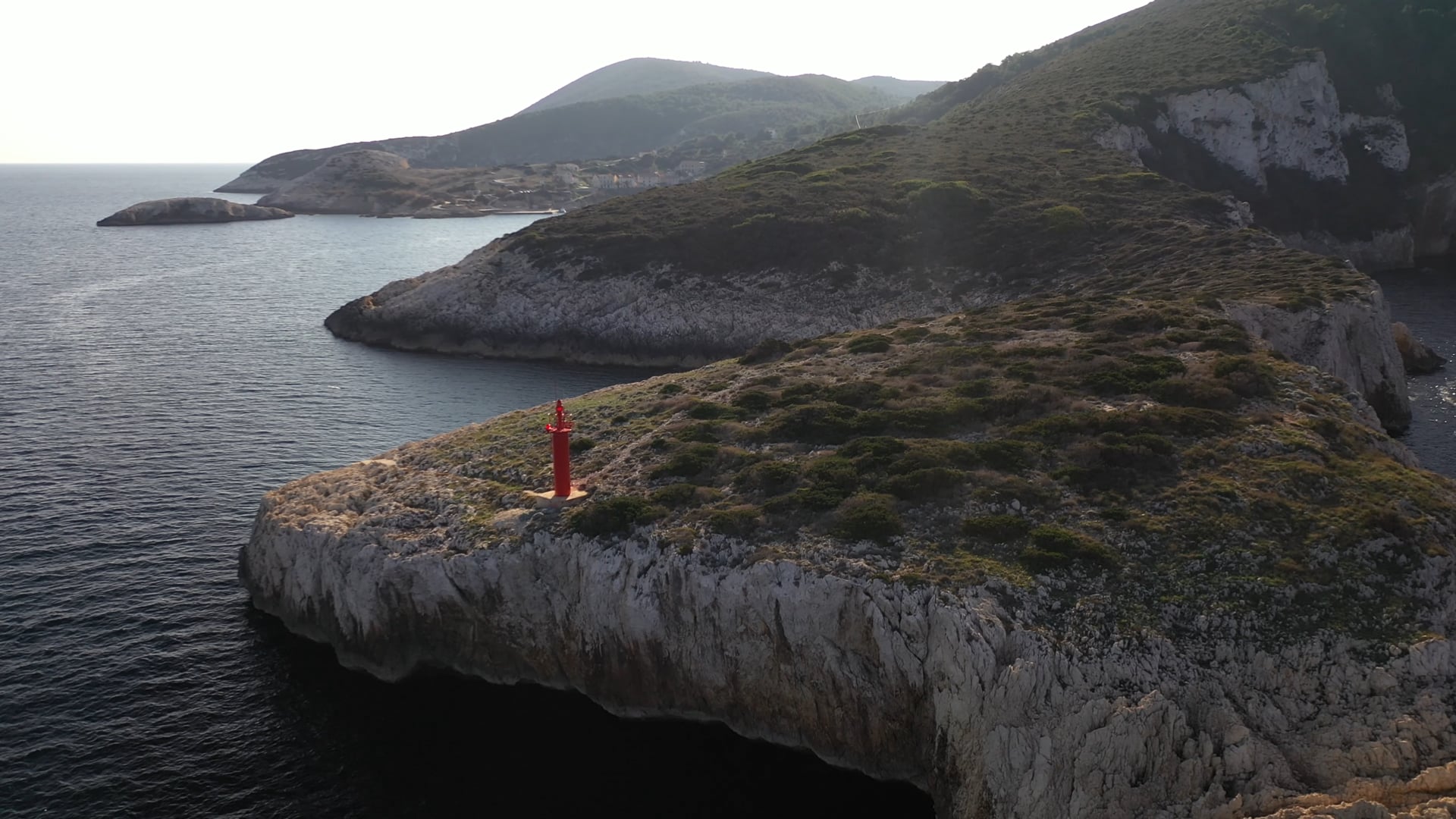 Approaching the small red lighthouse on the stone cliff, deep blue, calm sea