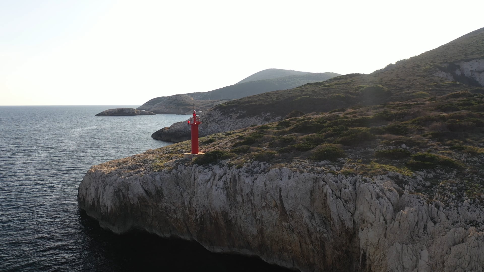 Moving by the small red lighthouse on the stone cliff, deep blue, calm sea, close up view, sunshine