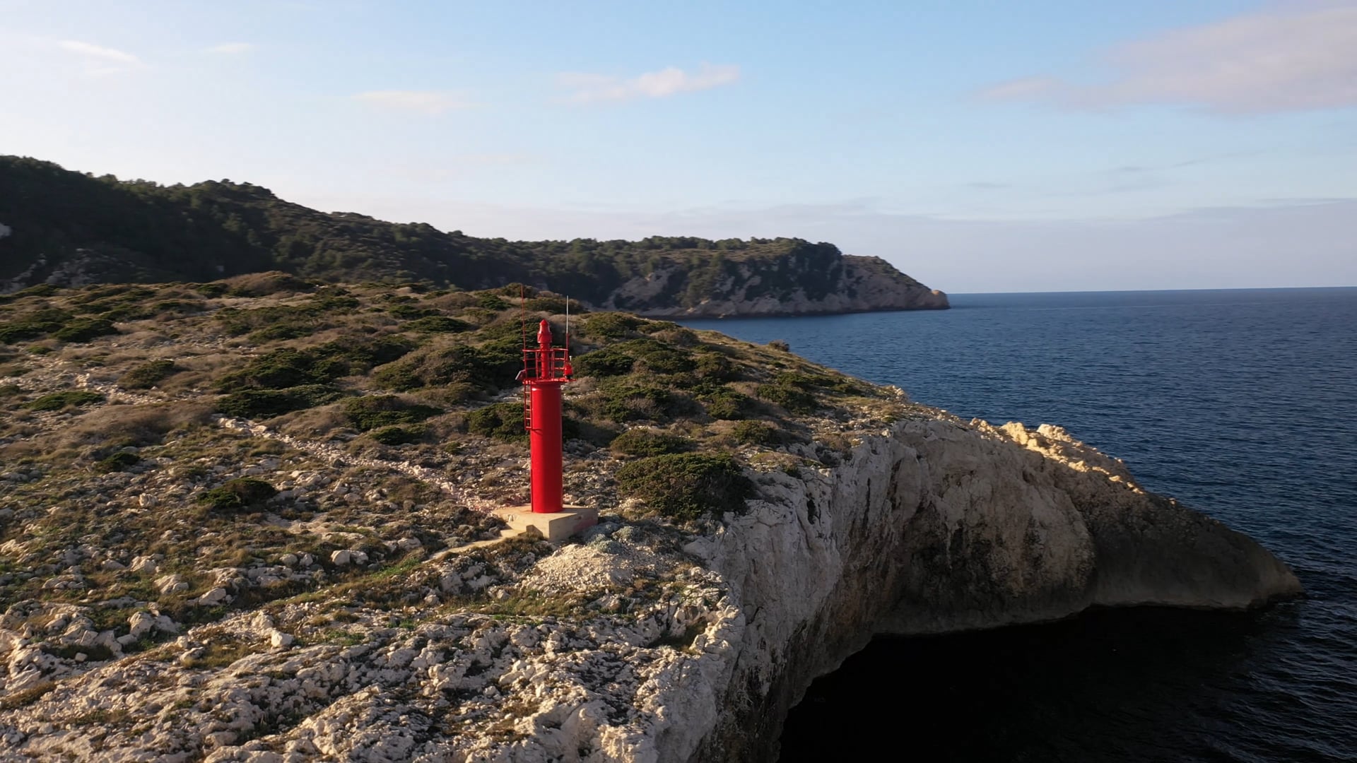 Small red lighthouse on the stone cliff, deep blue, calm sea, close up view