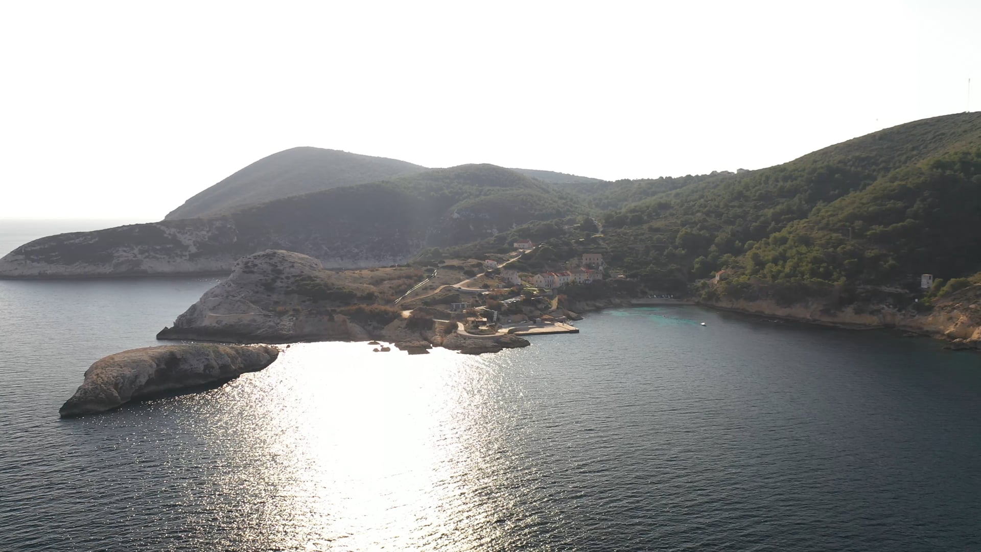 Sunshine, approaching and discovering beautiful small bay, dark blue and crystal clear sea, forest in the background