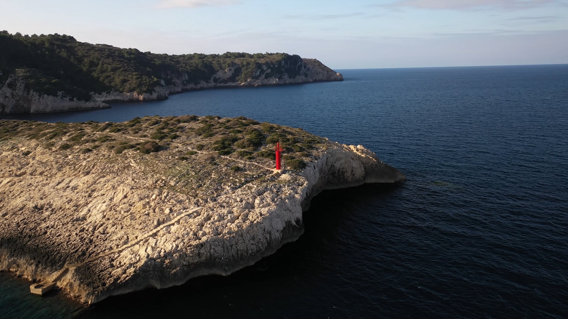 Small red lighthouse on the stone cliff, deep blue, calm sea