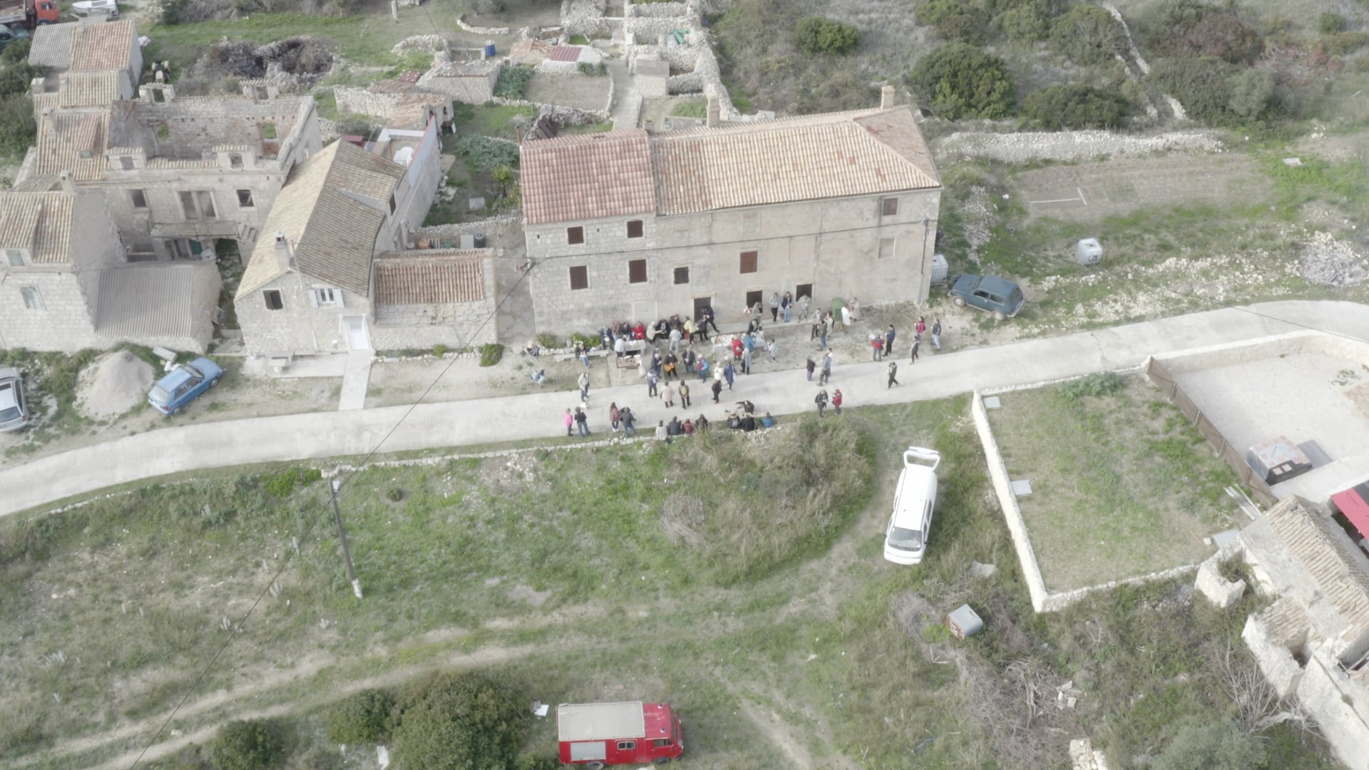 Top view, people standing, talking, having fun on the road in front of the house, stone walls visible in the background