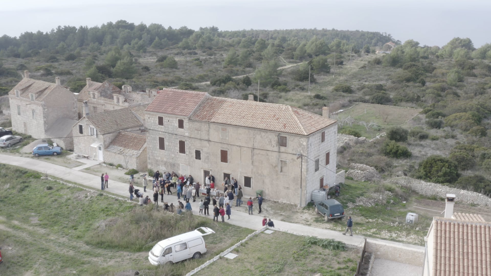 People standing, talking, having fun on the road in front of the house, few cars visible