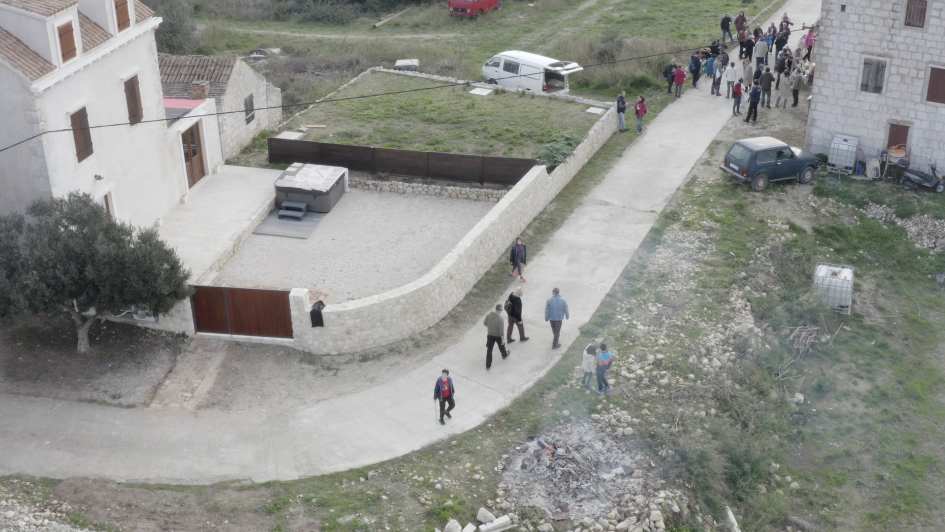 Smoke, people standing in front of the house, more people walking on the road, kids playing