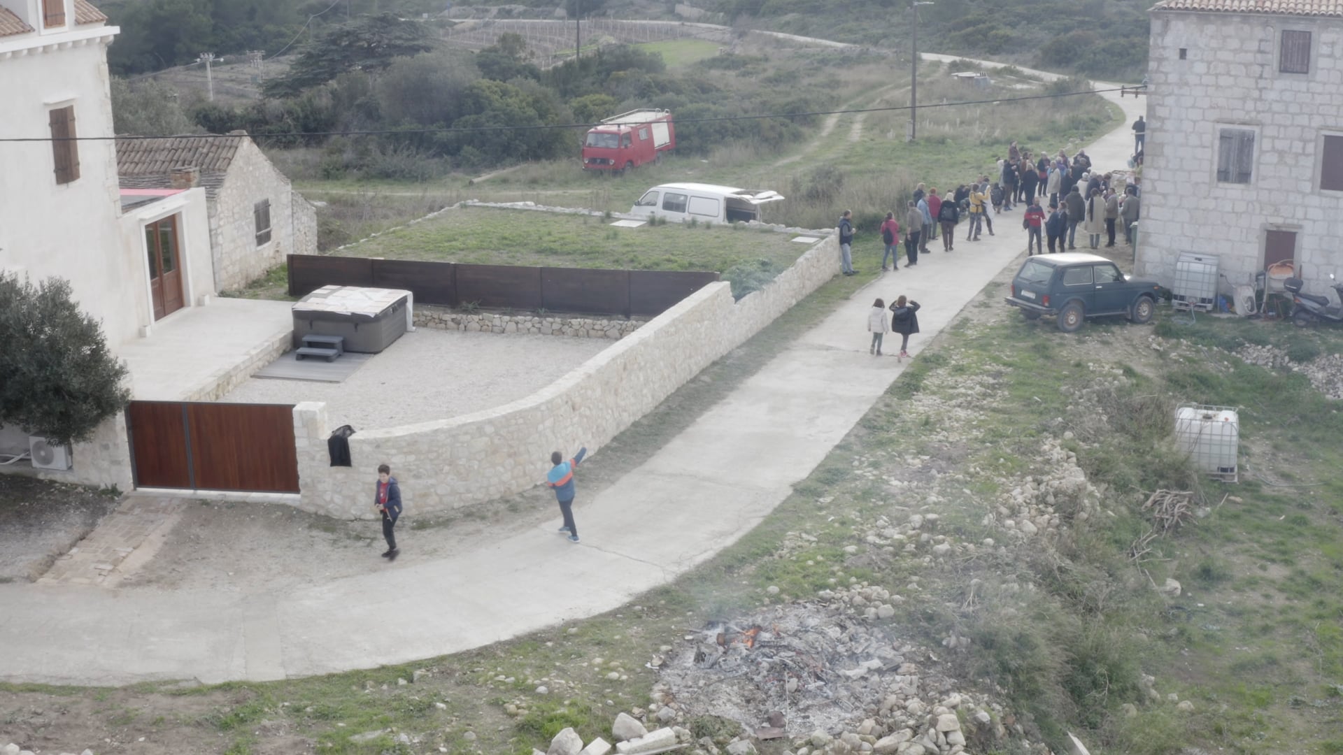 Kids playing with fire, smoke, a lot of people standing, talking, having fun in front of the stone house