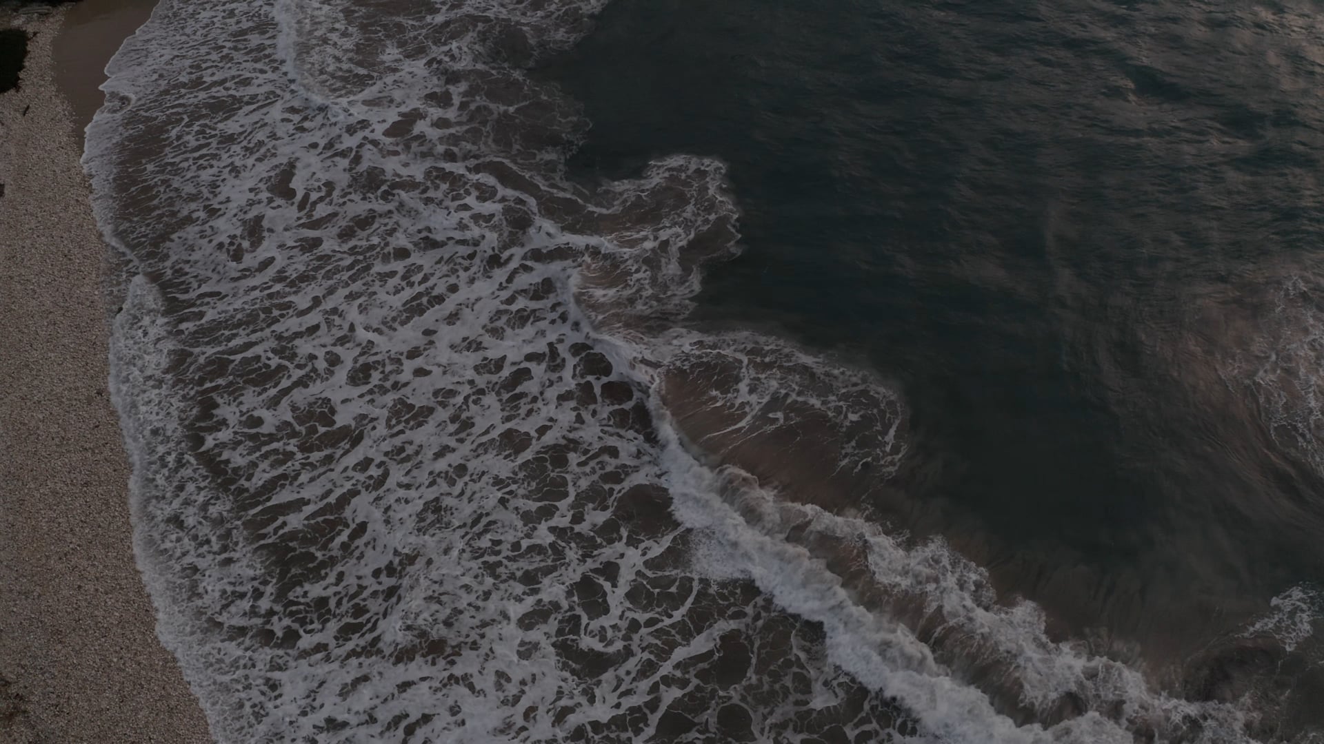 Waves splashing on the beach, foamy dark blue sea, sunshine reflecting on the water