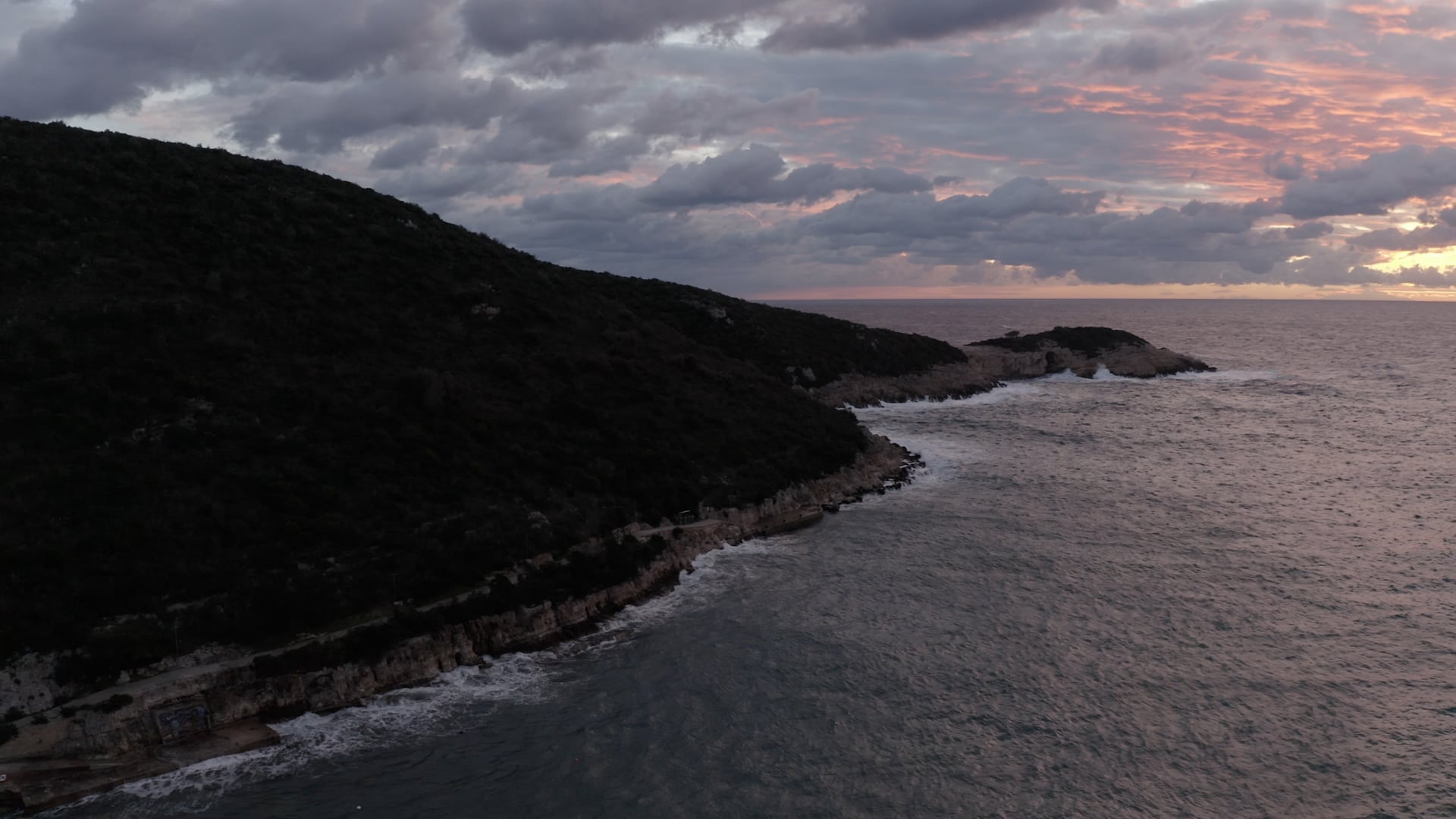 Beautiful sunset, colored sky, waves crashing the stone cliffs, turbulent dark blue sea