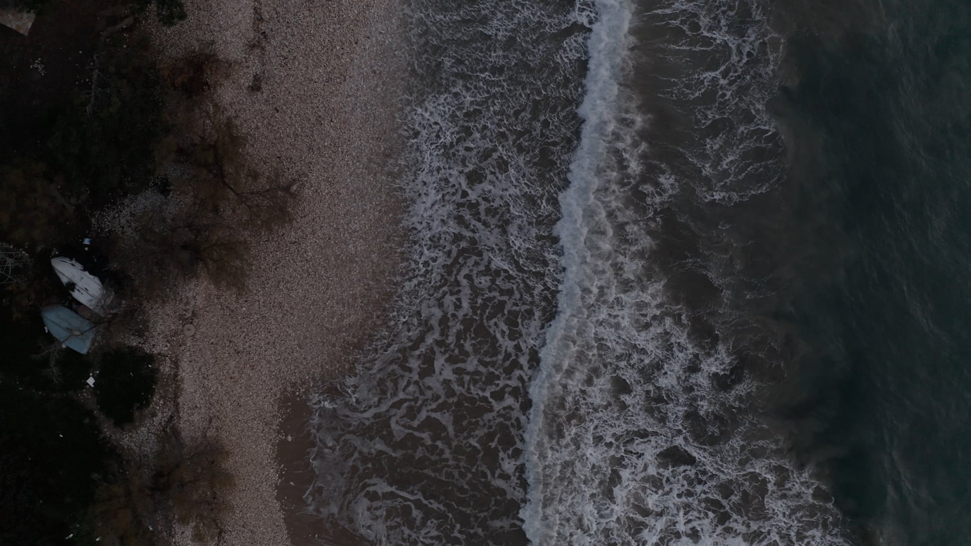 Waves splashing the pebble beach, top view, 2 boats sitting on the beach