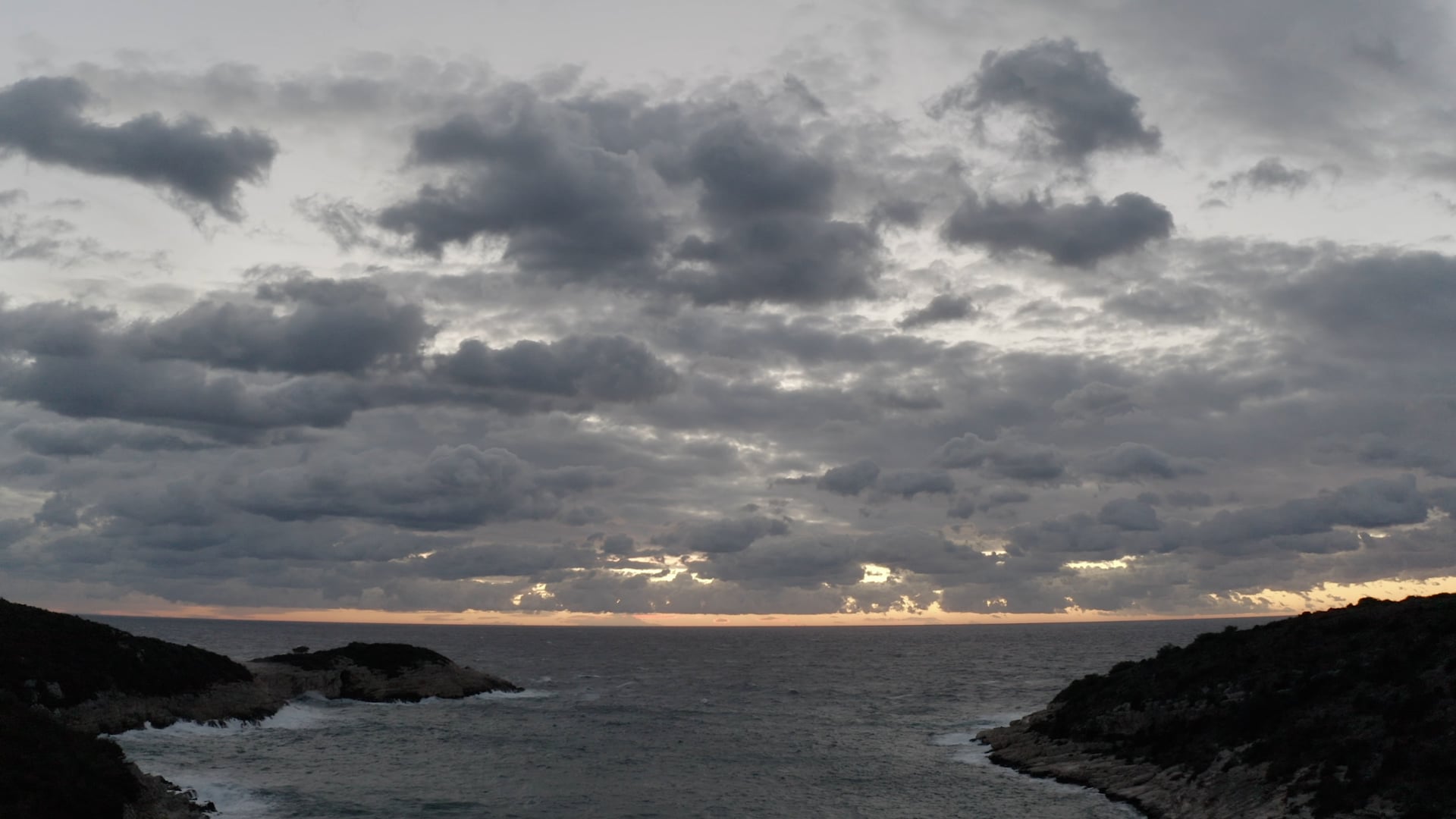 Rising above the turbulent sea, waves crashing at the stone cliffs, sunset in the background