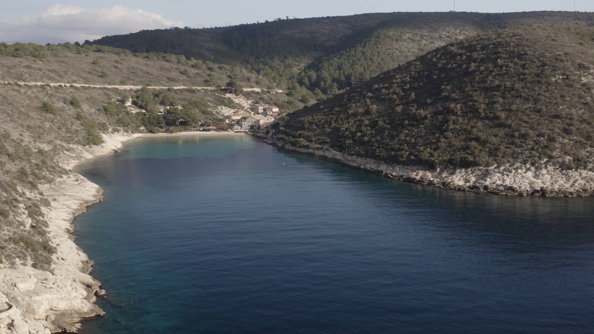Approaching few houses near the beach, forest in the background, crystal clear blue sea, road visible