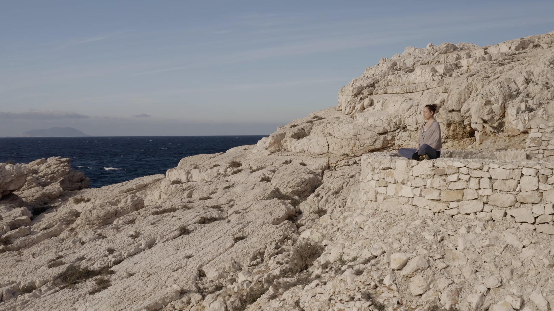 Woman sitting calmly and peacefully on the stone wall near the sea