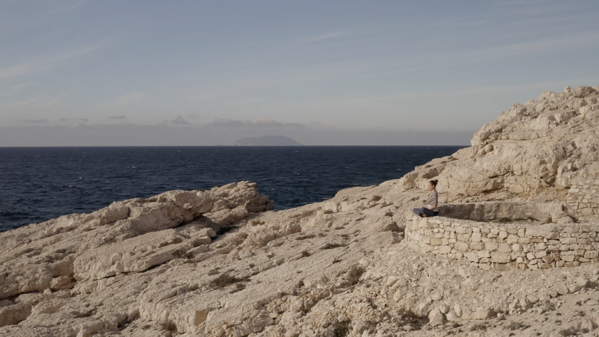 Woman sitting peacefully on the stone wall near the dark blue sea
