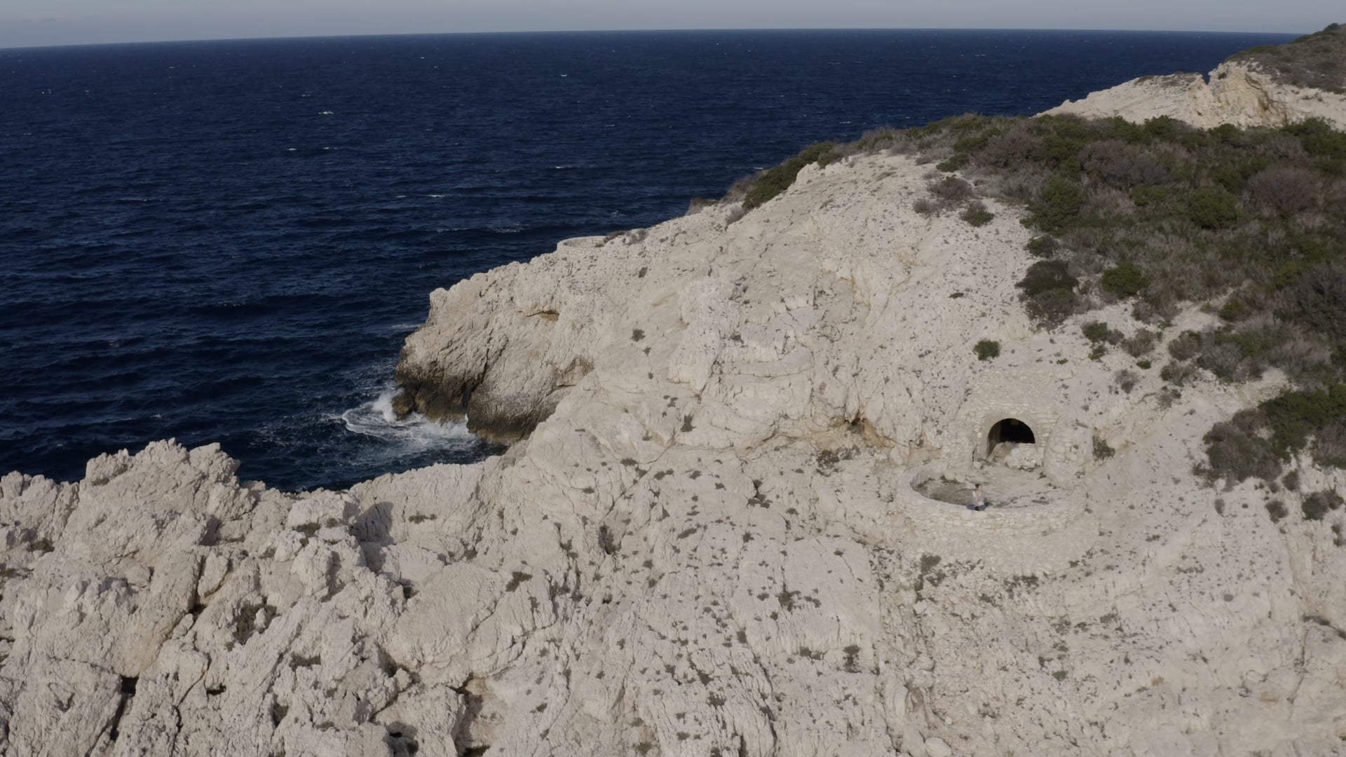 Waves splashing the cliff, woman sitting on the curved stone wall