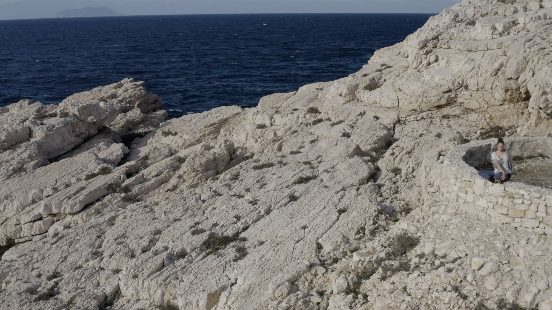 Woman stretching, doing yoga on the stones near the dark blue sea, sunshine