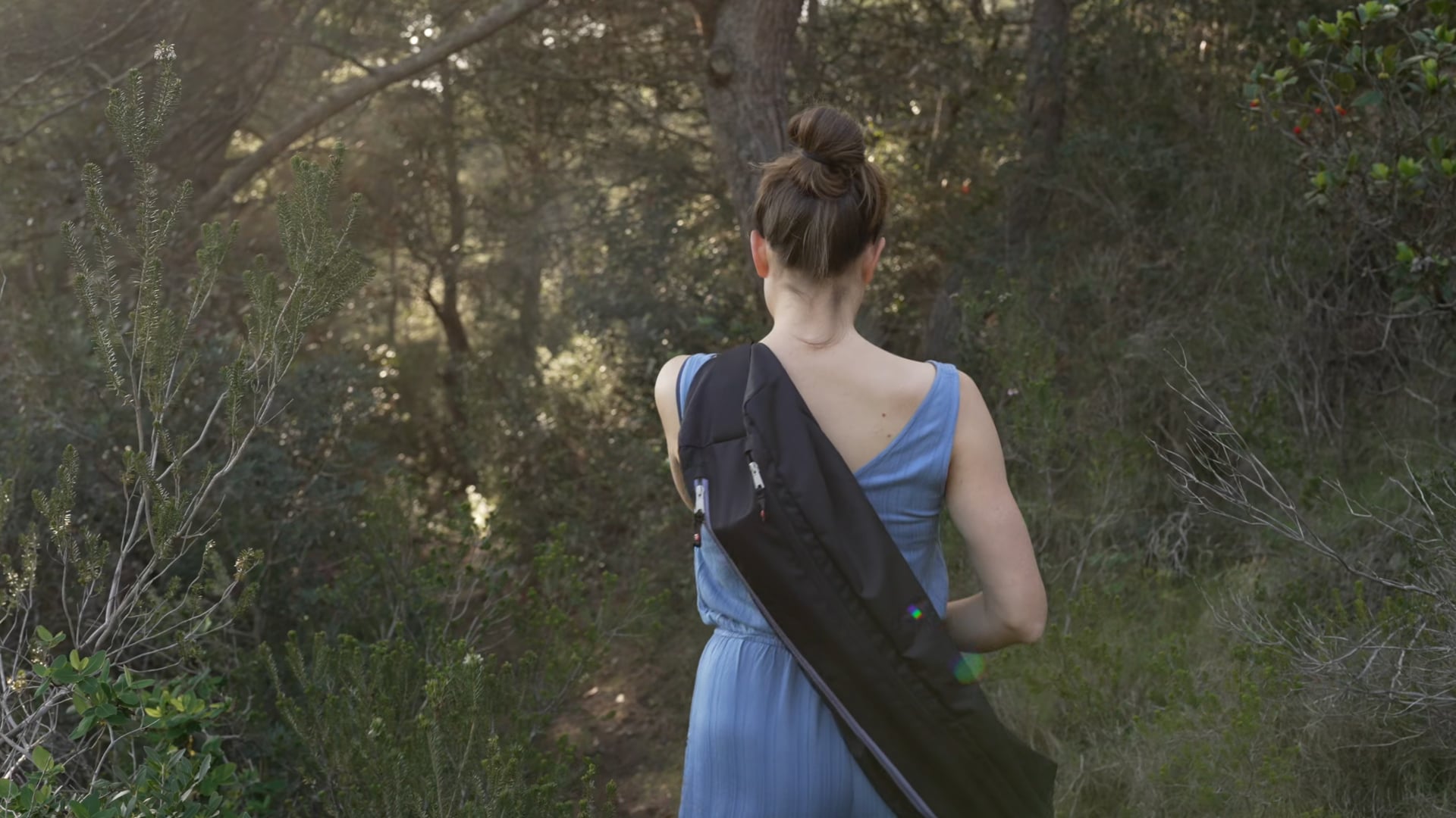 Woman walking through the green forest carrying a bag, close up shot, sunshine