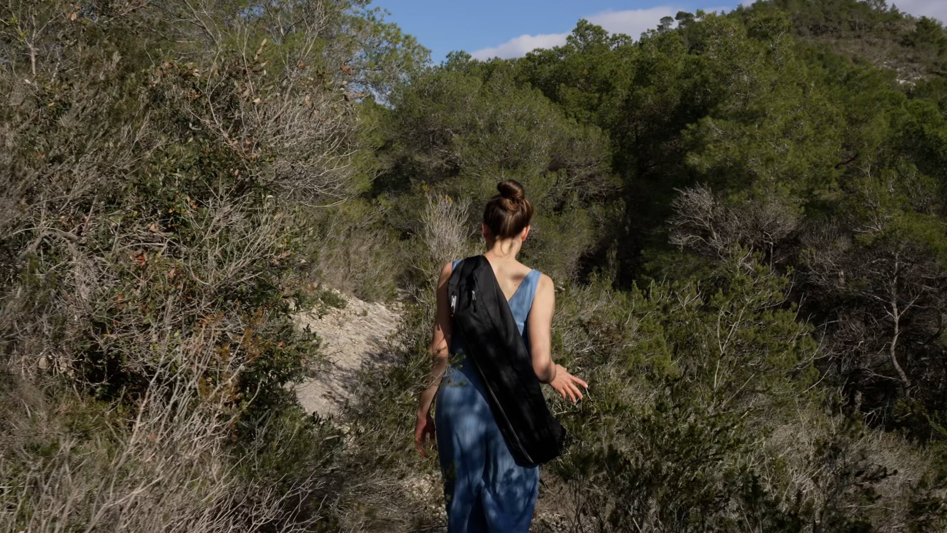 Woman carrying a bag walking through the forest, touching the bushes, close up view