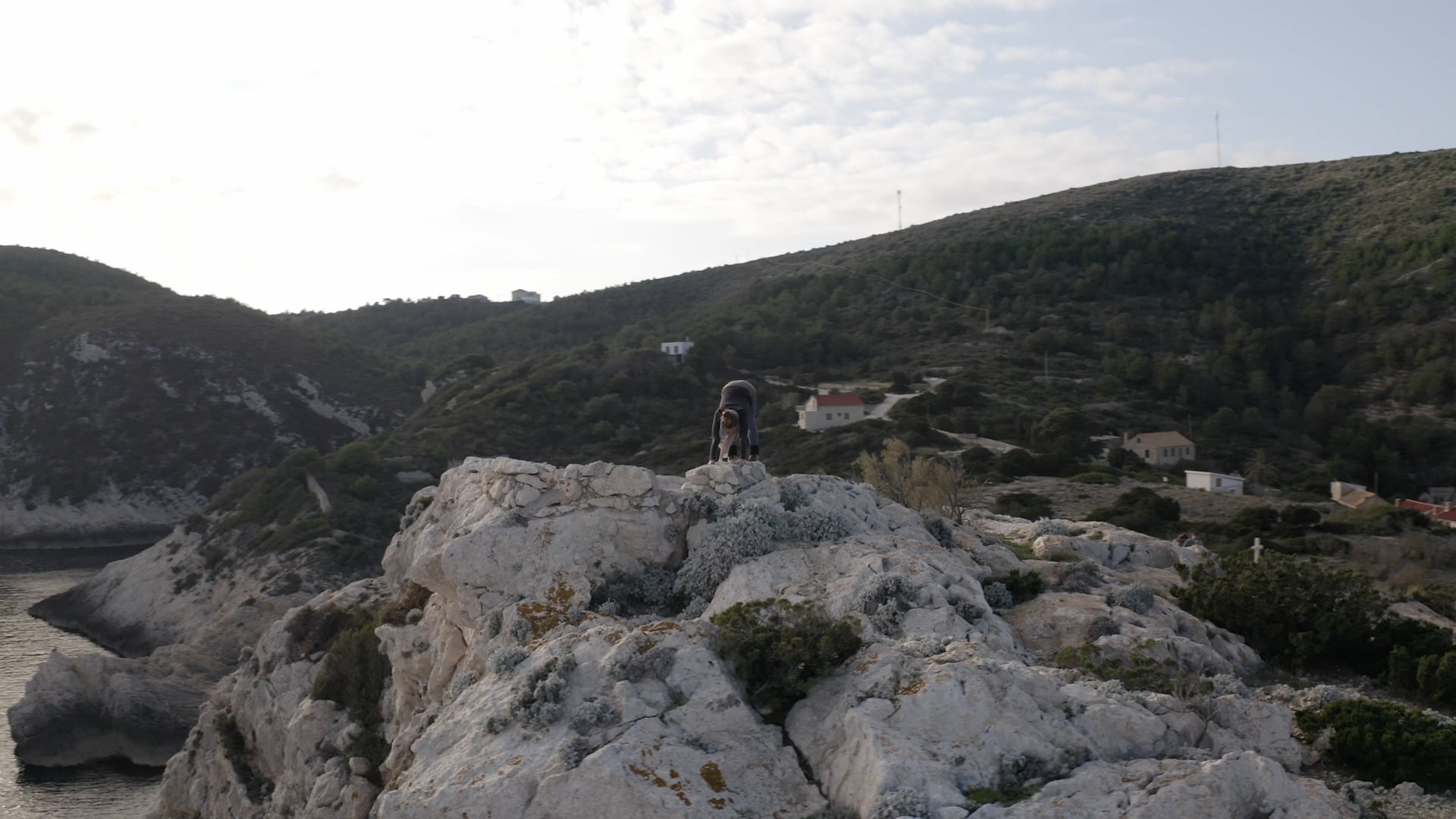 Woman doing yoga on the top of the cliff, forest and sea in the background, slow 360° view