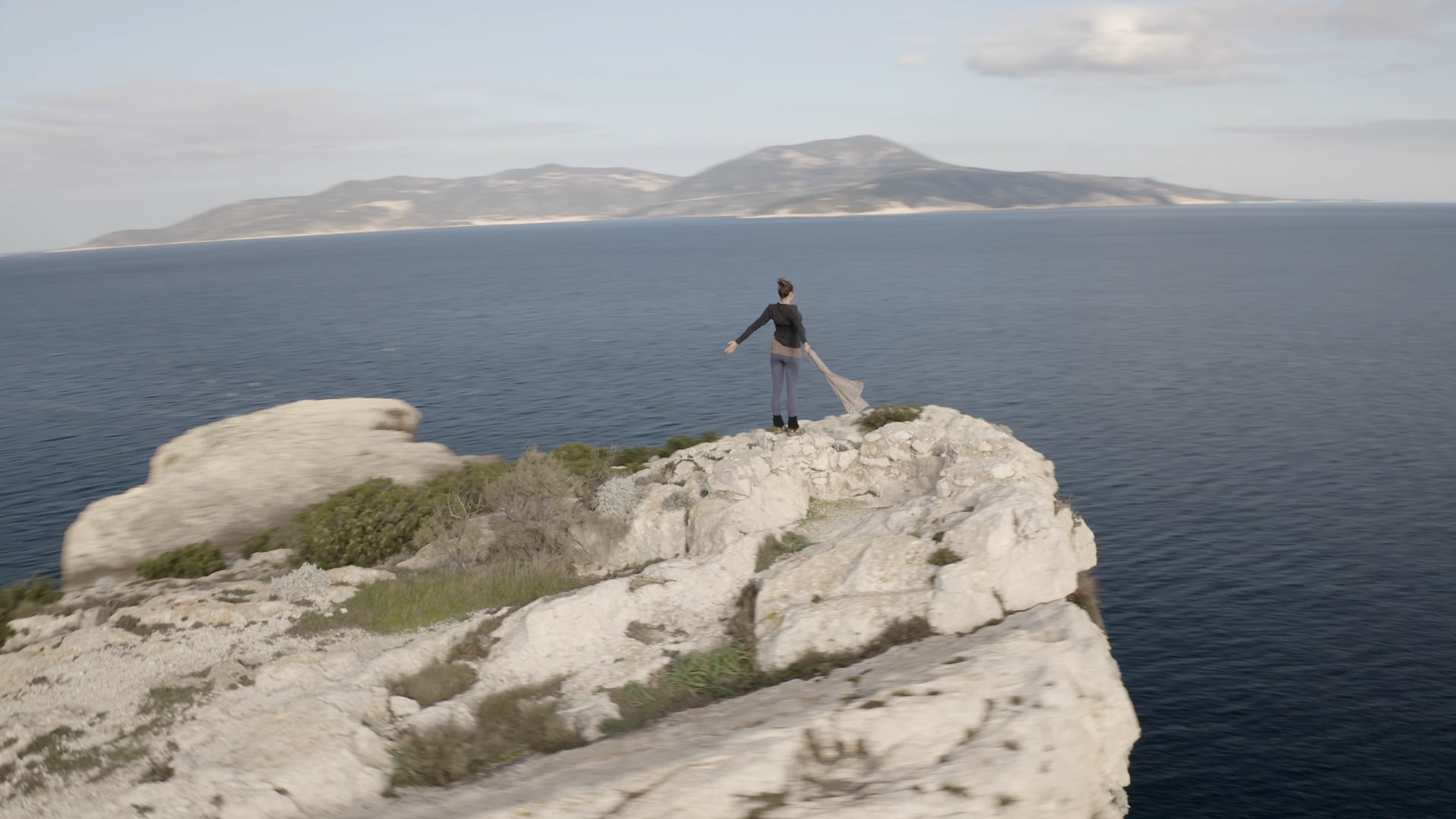 Woman streching on the top of the cliff with a scarf in her hand, windy weather