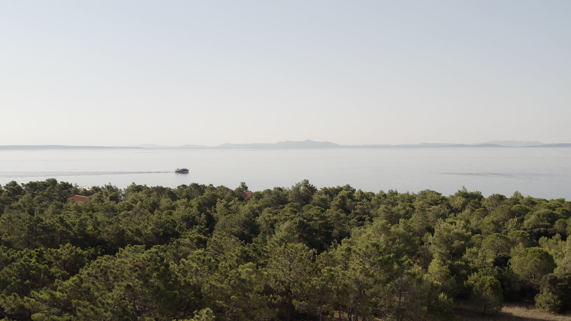 Boat slowly sailing to the right, other islands visible in the background