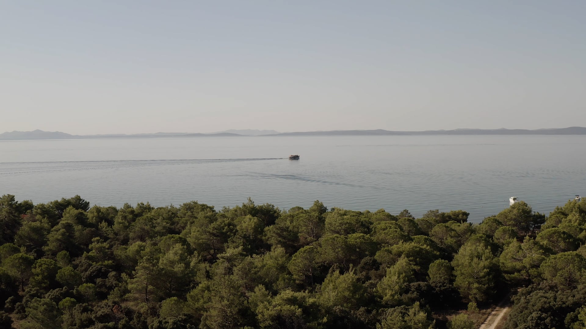 Boat slowly sailing in the sea, forest and islands visible on the horizon