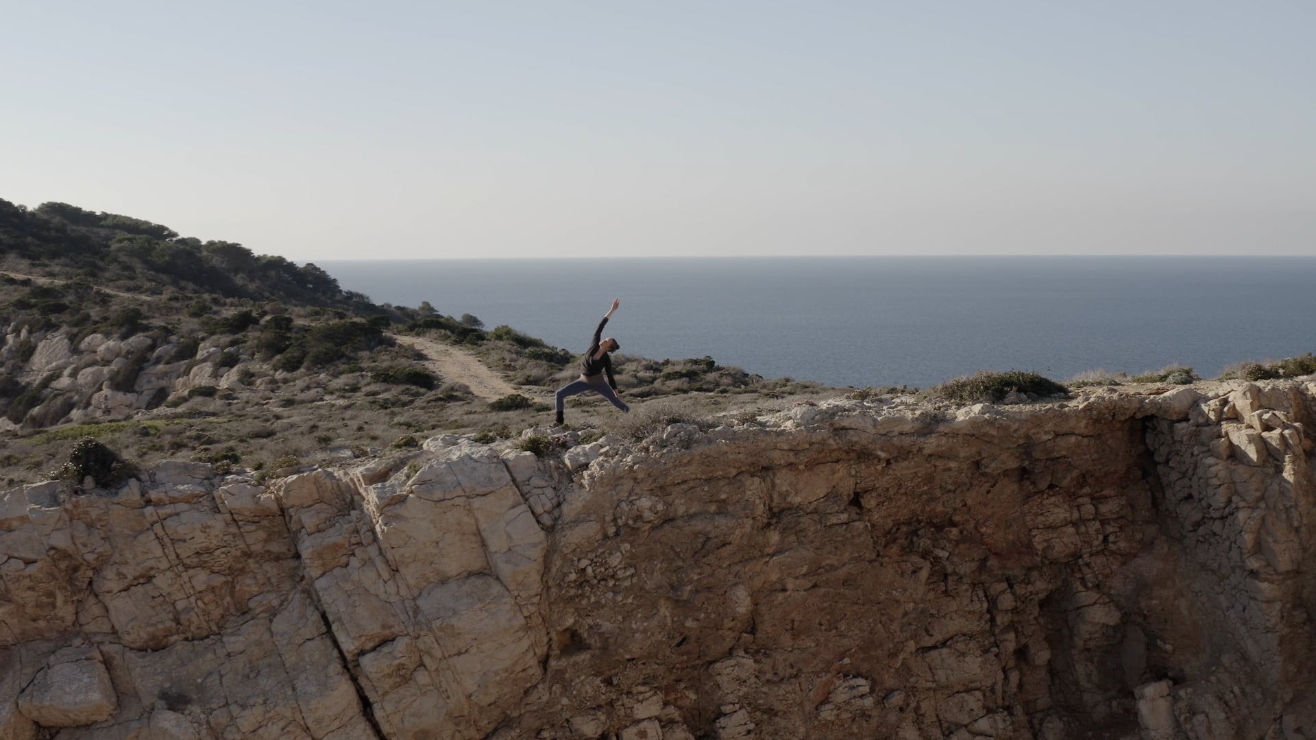 Woman practicing yoga at the top of the island, sea visible behind