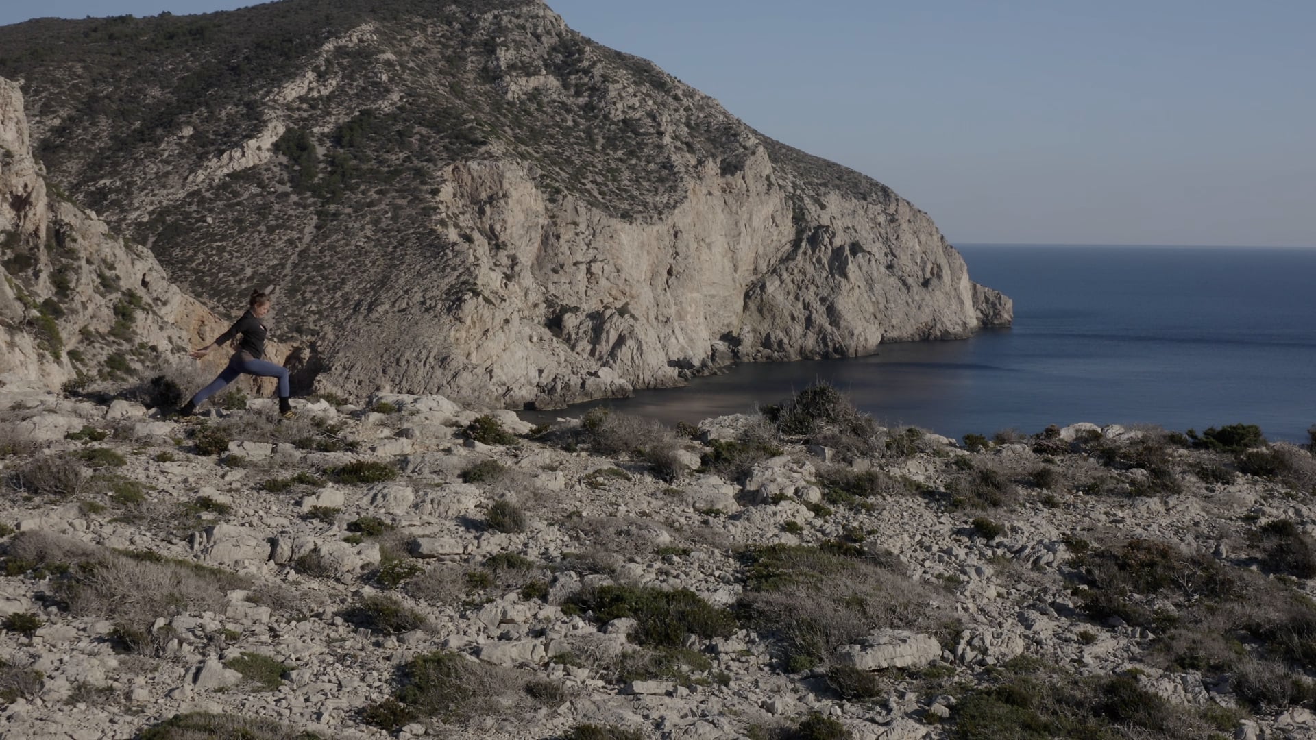 Woman practicing yoga at the top of the island, sun shining, sea and rocky island visble behind